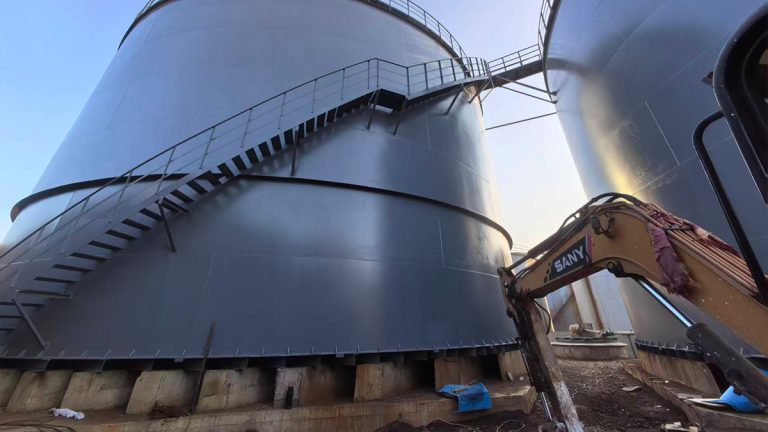 Row of large white vertical industrial storage tanks with safety ladders and top platforms by Shijie Heavy Industry
